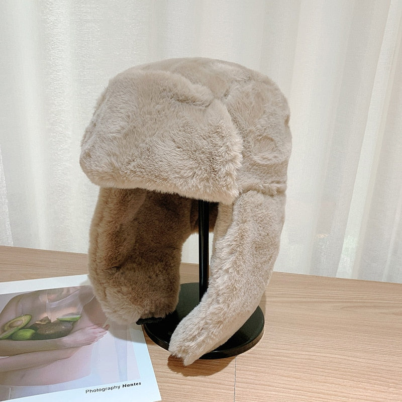 Kuschelige, beige Wintermütze aus Kunstpelz mit Ohrenklappen auf einem Tisch. Perfekt für kalte Tage, modisch und warm. Ideal für Wintermode.