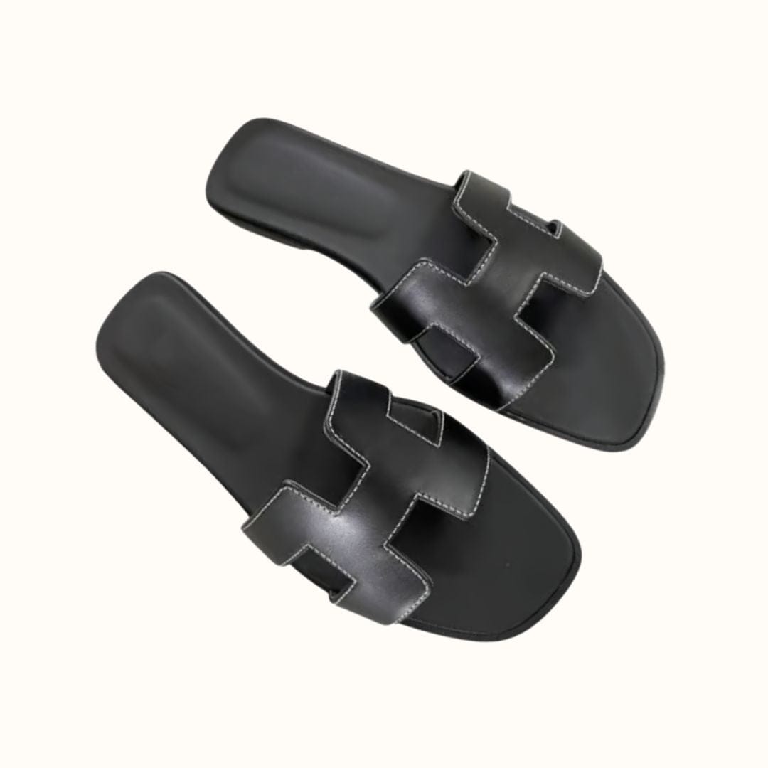 Schwarze Ledersandalen mit markantem H-Design, flachem Absatz und weißen Nähten. Perfekt für Sommermode und lässige Outfits.