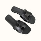 Schwarze Ledersandalen mit markantem H-Design, flachem Absatz und weißen Nähten. Perfekt für Sommermode und lässige Outfits.