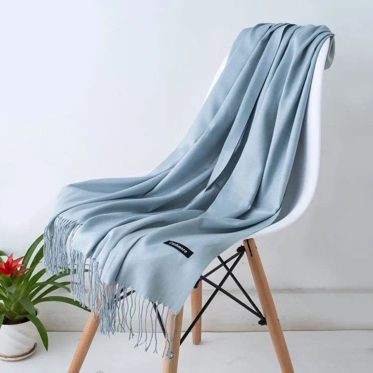 Eleganter hellblauer Schal aus Kaschmir, weich und luxuriös, drapiert über einem modernen Stuhl. Perfekt für stilvolle Herbst- und Wintermode.