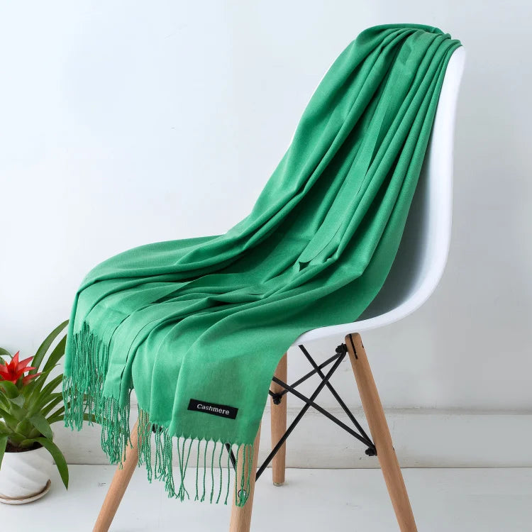 Grüner Kaschmirschal auf weißem Stuhl, luxuriös und weich, ideal für stilvolle Wintermode. Perfekt als Geschenk oder für den persönlichen Gebrauch.
