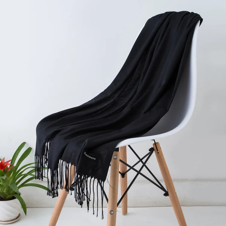 Schwarzer Schal aus Kaschmir auf weißem Stuhl, elegantes Design, weiche Textur, ideal für Herbstmode. Perfekt als stilvolles Accessoire.