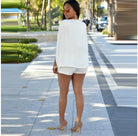 Frau in eleganter weißer Kleidung und High Heels auf sonniger Promenade. Sommermode, stilvolle Outfits, urbane Eleganz, modische Accessoires.