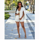 Elegantes weißes Sommeroutfit für Damen: Kurzer Jumpsuit mit Cape, kombiniert mit High Heels und Sonnenbrille. Perfekt für stilvolle Anlässe.