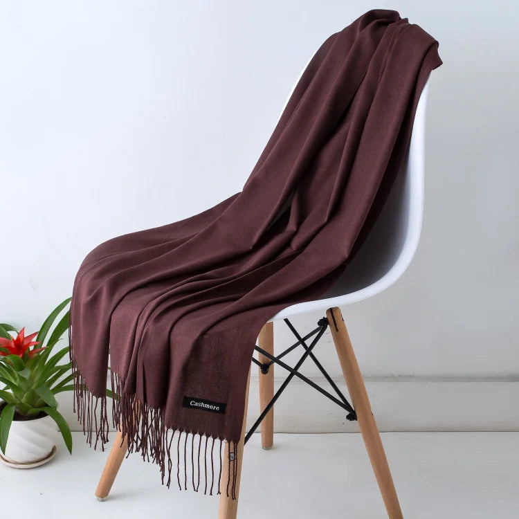 Luxuriöses braunes Kaschmirschal auf modernem Stuhl, ideal für stilvolle Herbst- und Wintermode. Weich, warm und elegant. Perfektes Accessoire.