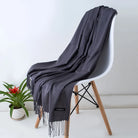 Grauer Kaschmirschal auf weißem Stuhl, elegantes Design, weiche Textur, ideal für Herbst und Winter. Perfekt als modisches Accessoire.
