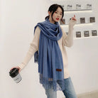 Frau mit blauem Schal und Kaffeebecher, trägt cremefarbenen Pullover und Jeans. Modetrend, Herbstmode, Damenaccessoires, lässiger Stil.