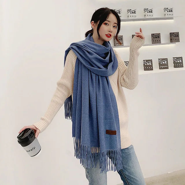 Frau mit blauem Schal und Kaffeebecher, trägt cremefarbenen Pullover und Jeans. Modetrend, Herbstmode, Damenaccessoires, lässiger Stil.