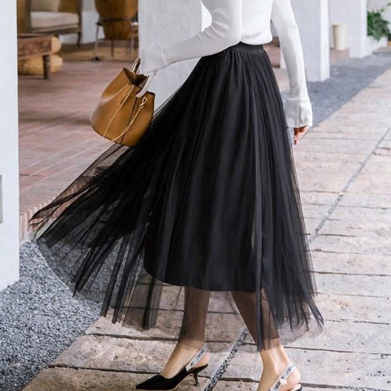 Eleganter schwarzer Tüllrock kombiniert mit weißen Pumps und brauner Handtasche. Perfekt für stilvolle Damenmode und trendige Outfits.