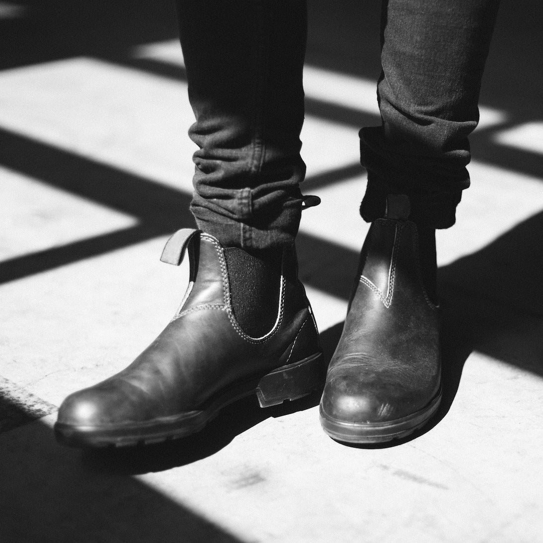 Schwarze Chelsea Boots aus Leder, getragen von Person in Jeans. Stilvolle, zeitlose Schuhe für Herrenmode, ideal für urbanen Look.