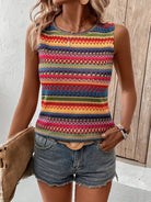 Frau trägt buntes, ärmelloses Ethno-Top mit geometrischem Muster und Jeansshorts. Sommermode, Boho-Stil, lässiger Look, Damenbekleidung.