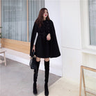 Elegantes schwarzes Cape-Kleid für Damen, kombiniert mit Overknee-Stiefeln und Handtasche. Perfekt für stilvolle Herbst- und Wintermode.