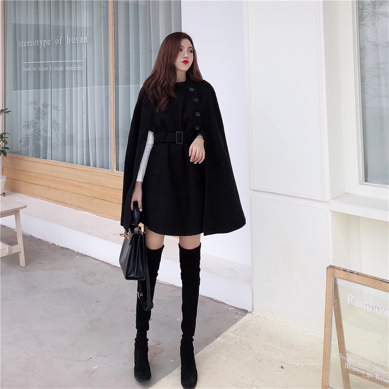 Elegantes schwarzes Cape-Kleid für Damen, kombiniert mit Overknee-Stiefeln und Handtasche. Perfekt für stilvolle Herbst- und Wintermode.