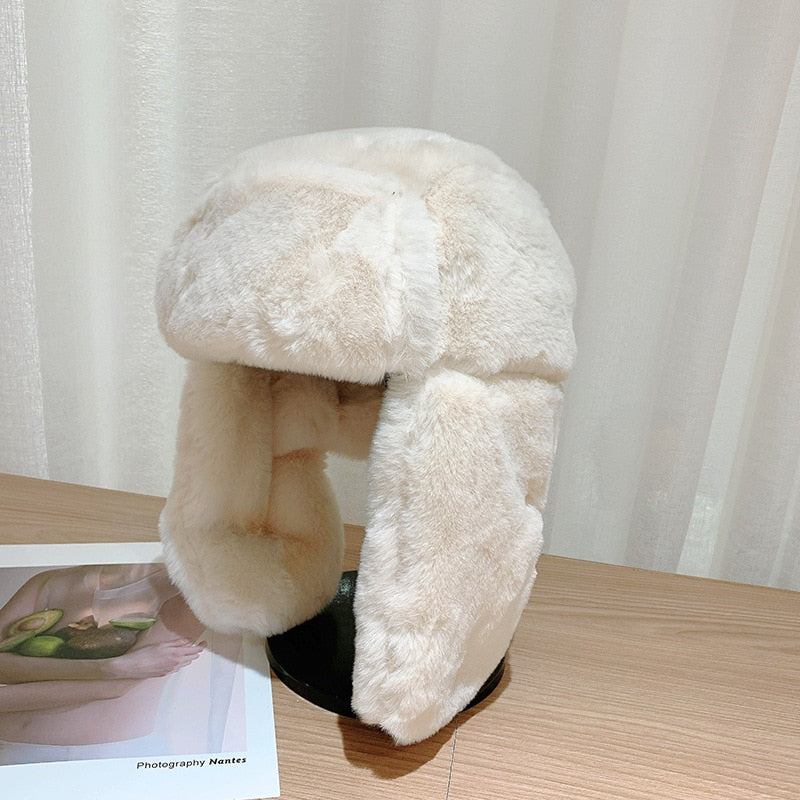 Kuschelige, weiße Kunstpelz-Fliegermütze auf Holztisch vor Vorhang. Wintermode, warme Accessoires, stilvolle Kopfbedeckung.
