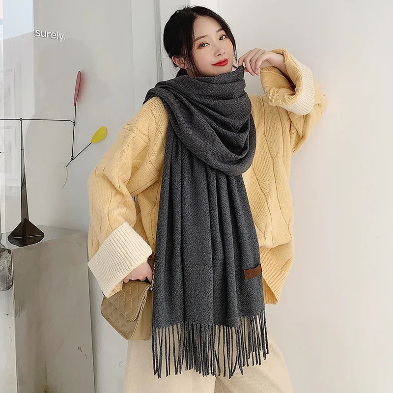 Damenmode: Eleganter, grauer Schal mit Fransen, kombiniert mit beigem Strickpullover. Perfekt für Herbst und Winter. Trendig und stilvoll.