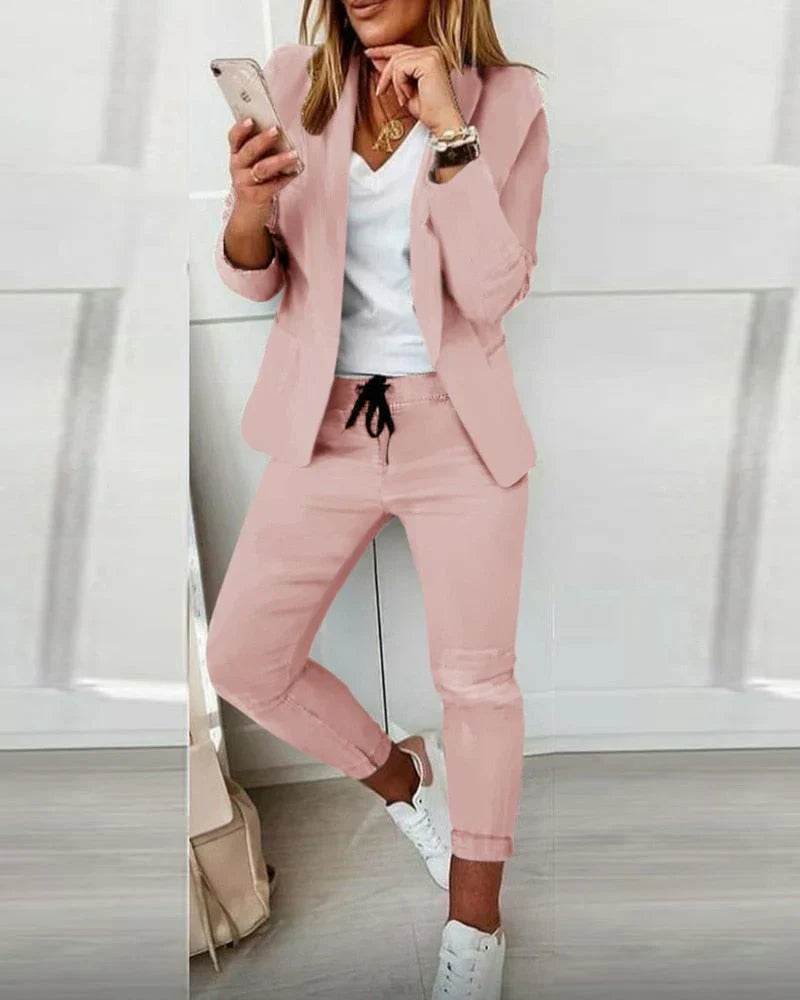 Damenanzug in Rosa, bestehend aus Blazer und Jogginghose, kombiniert mit weißem T-Shirt und Sneakers. Modischer Freizeitlook für Frauen.
