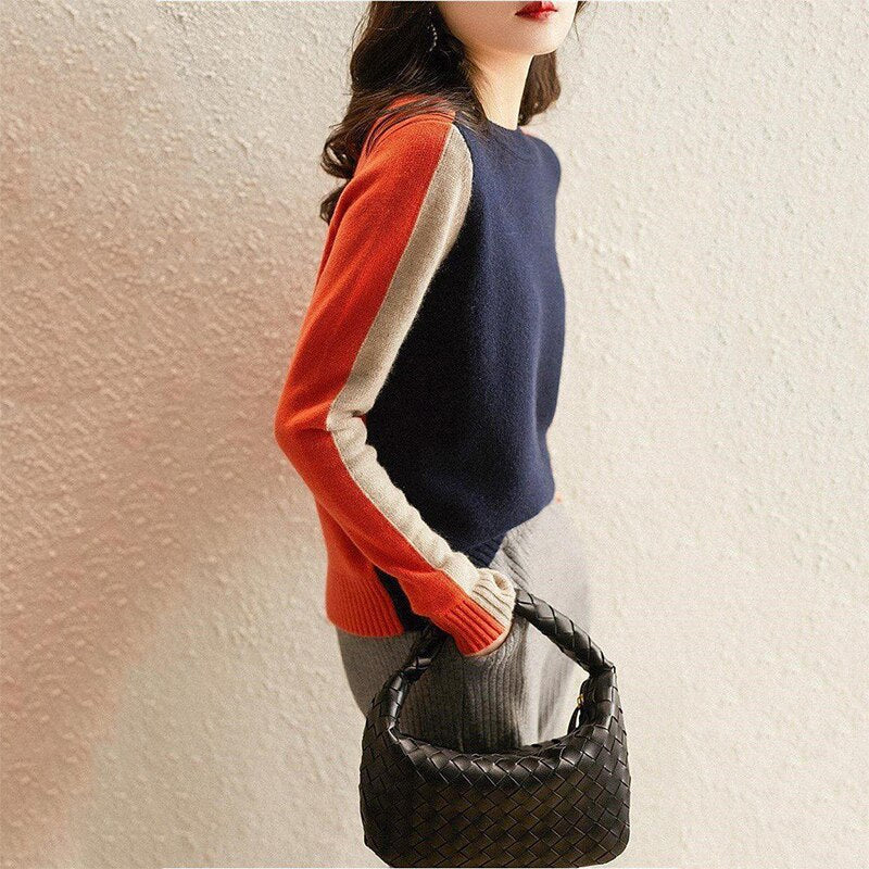 Damenpullover in Blau mit roten und beigen Ärmeln, kombiniert mit einer schwarzen geflochtenen Handtasche. Modischer Herbst-Look.