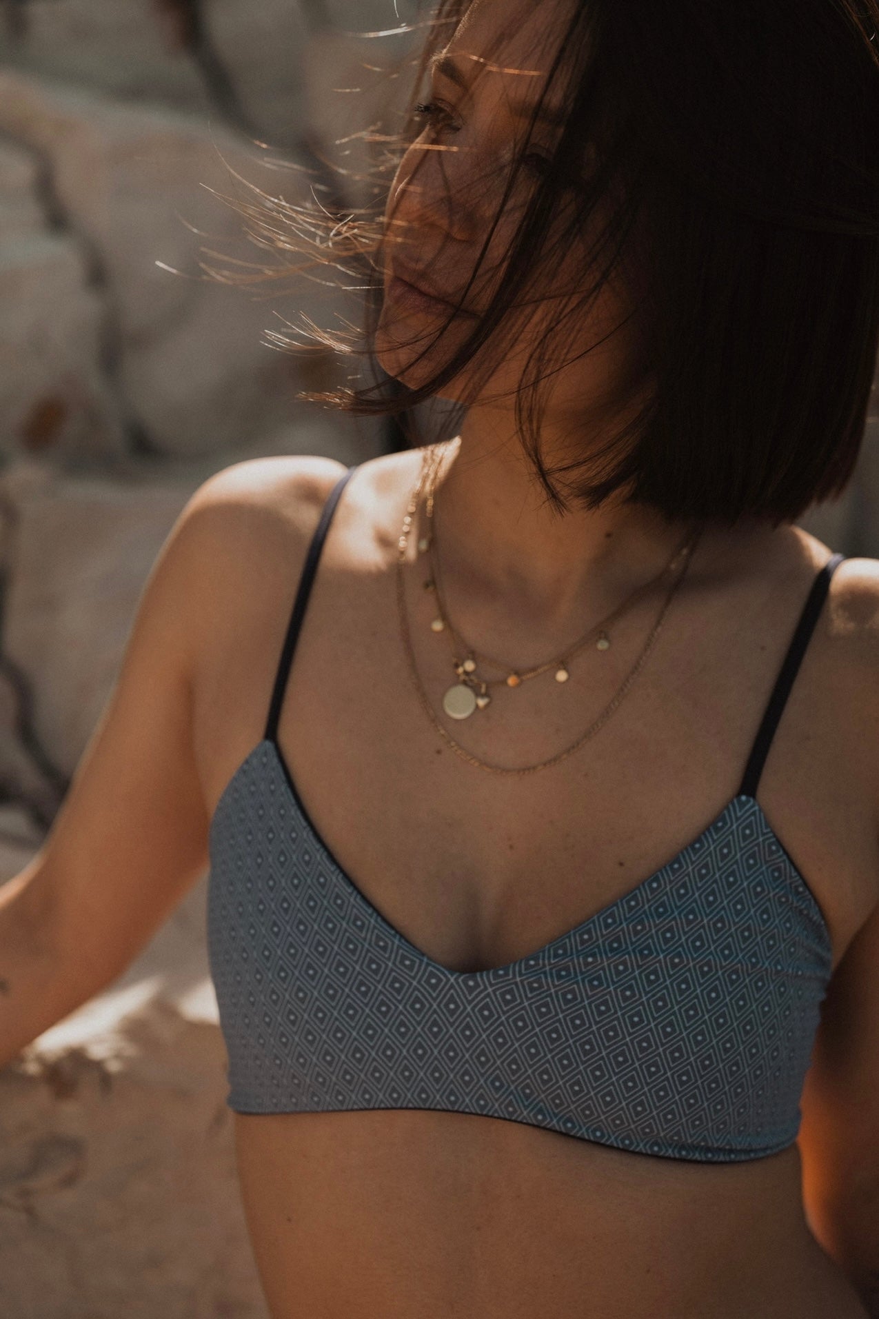 Frau in blauem Bikini-Oberteil mit geometrischem Muster, trägt Halsketten, Sommermode.