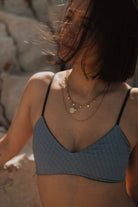 Frau in blauem Bikini-Oberteil mit geometrischem Muster, trägt Halsketten, Sommermode.