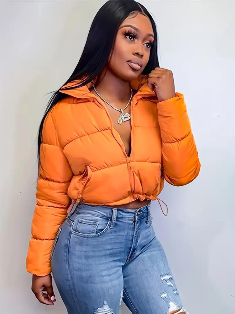 Frau in orangefarbener Steppjacke und zerrissenen Jeans. Modetrend, Winterjacke, Streetwear, Damenmode, stilvoll, lässig, urban.