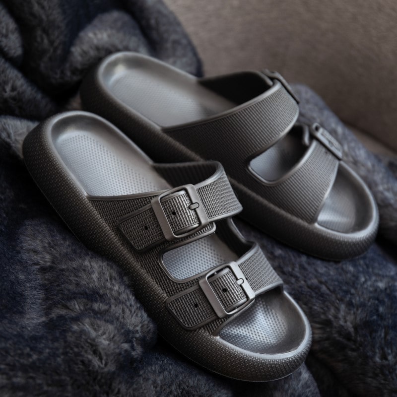 Graue Sandalen mit doppelten Schnallen auf weichem, dunklem Stoff. Bequeme Sommerschuhe, ideal für Freizeit und Strand.