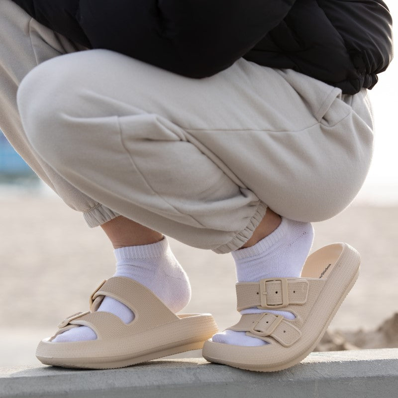 Beige Sandalen mit zwei Schnallen, getragen mit weißen Socken. Komfortable Sommerschuhe, ideal für Strand und Freizeit. Trendige Modeaccessoires.