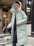 Frau in stilvollem, hellblauem Daunenmantel, kombiniert mit schwarzer Hose und Designer-Handtasche. Wintermode, urbane Eleganz, Streetstyle.