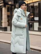 Frau in langem, hellblauem Daunenmantel und Mütze auf städtischer Straße. Wintermode, stilvoll, warm, modischer Mantel, Outdoor-Bekleidung.