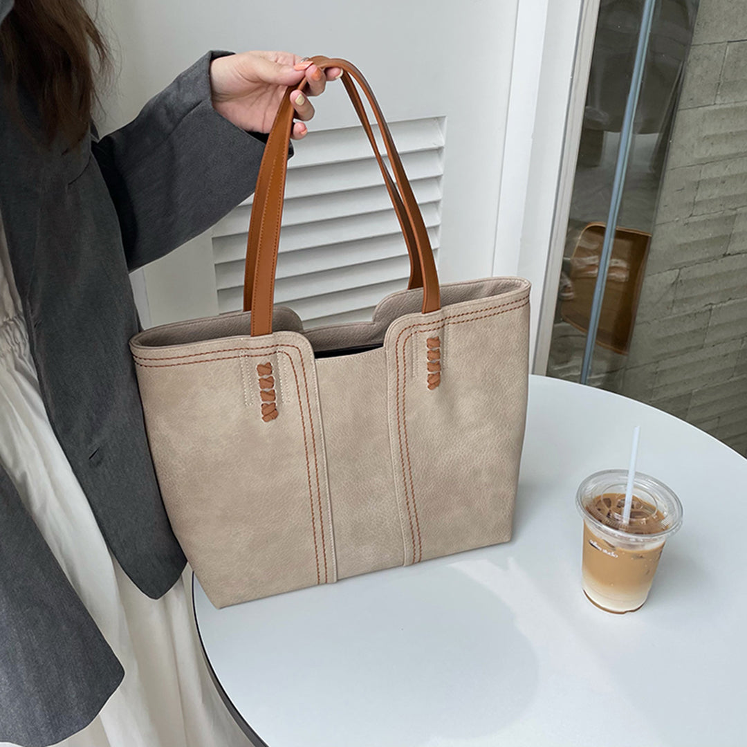 Elegante beige Handtasche mit braunen Griffen auf weißem Tisch, neben einem Eiskaffee. Perfekt für stilvolle Damenmode und Accessoires.