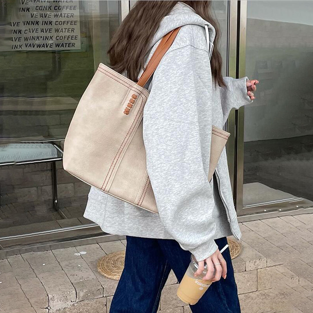 Frau mit grauem Hoodie und beiger Ledertasche, hält Eiskaffee. Modetrend, lässiger Streetstyle, stilvolle Accessoires, urbaner Look.