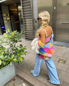 Frau in bunter Patchwork-Strickjacke, kombiniert mit blauer Jeans und weißem Top. Modische Herbst-Winter Streetwear für Damen.