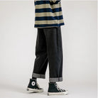 Weite Herrenjeans im Baggy-Stil, ideal für Streetwear. Dunkle Denim-Hose mit umgeschlagenem Saum, kombiniert mit gestreiftem Oberteil und Sneakers.