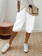 Frau in weißen Leinen-Bermudashorts, beige Umhängetasche, weiße Sneaker, lässiger Sommerlook.