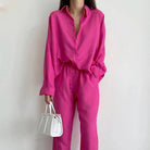 Frau in pinkem Leinen-Set mit Bluse und weiten Hosen, hält weiße Handtasche. Modetrend, Damenmode, Sommeroutfit, stilvoll, elegant.
