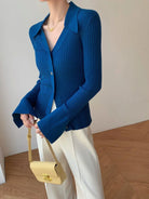 Blauer Strick-Cardigan mit langen Ärmeln und großem Kragen, kombiniert mit weißer Hose und gelber Handtasche. Elegante Damenmode, Vintage-Stil.