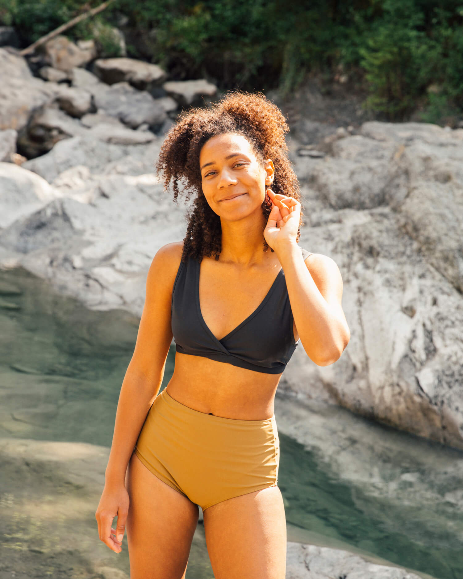 Frau im schwarzen Bikini-Top und moosgrüner Bikinihose am Flussufer, Sommermode.