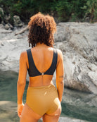 Frau im schwarzen Bikini-Top und moosgrünem Bikini-Höschen am Flussufer, Sommermode.