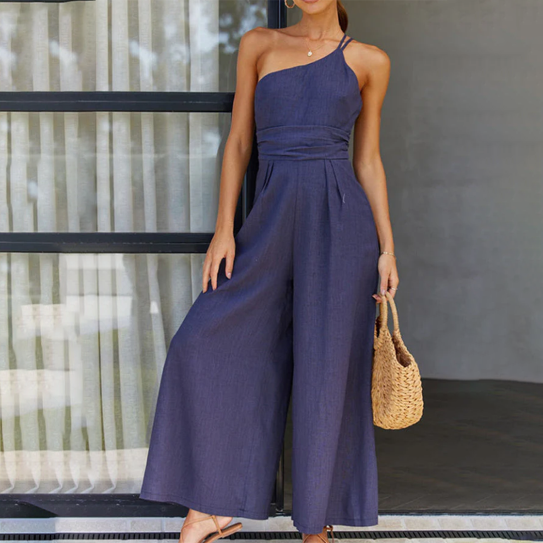 Frau in navyblauem Jumpsuit aus Leinen, schulterfrei, mit Strohtasche, Sommermode.