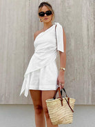 Frau in weißem, schulterfreiem Kleid mit Sonnenbrille und Strohtasche. Sommermode, eleganter Look, trendige Accessoires, stilvolle Kleidung.