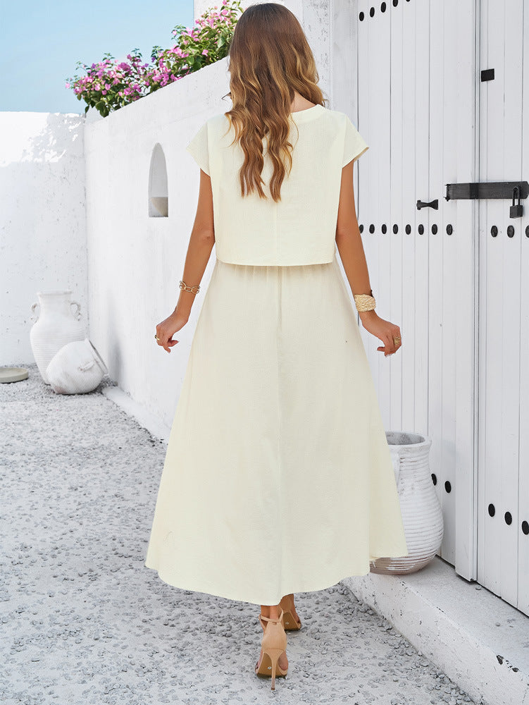 Frau in elegantem, cremefarbenem Maxikleid, steht auf mediterraner Terrasse. Sommermode, Damenkleidung, stilvoll, modern, luftiges Design.