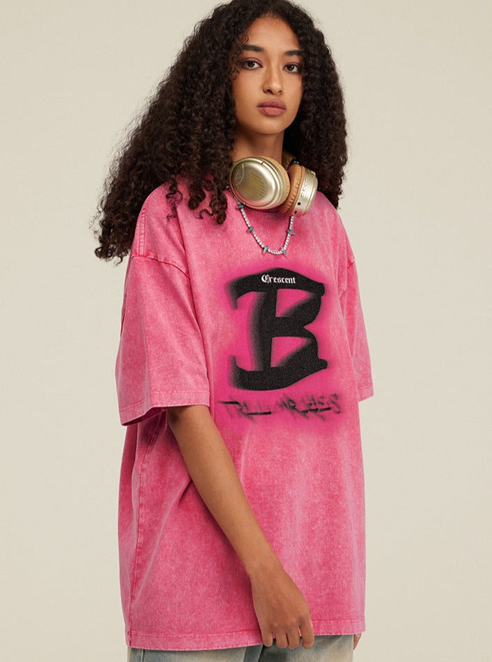 Rosa Oversize-T-Shirt mit großem "B"-Logo, getragen von Frau mit Kopfhörern. Modetrend, Streetwear, lässiger Stil, urbaner Look.
