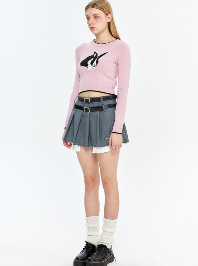 Junge Frau in modischem Outfit: rosa Pullover mit Pinguin-Design, grauer Faltenrock, weiße Socken, schwarze Schuhe. Trendige Damenmode 2023.