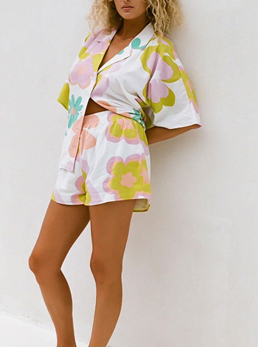Frau in geblümtem Sommer-Set aus Hemd und Shorts, pastellfarben, lässiger Stil, ideal für Strandmode und Freizeitkleidung.