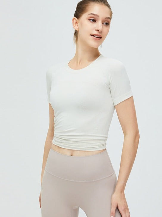 Damen-Sportoutfit: Weißes, kurzärmeliges Crop-Top kombiniert mit beigen Leggings. Perfekt für Yoga, Fitness und Freizeit. Bequem und stilvoll.
