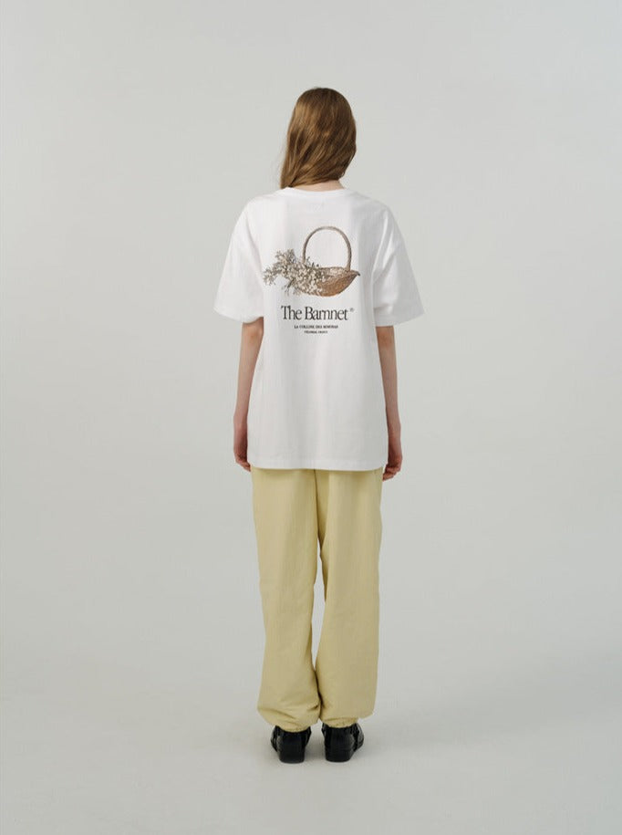 Weiße T-Shirt-Rückansicht mit floralem Design und "The Romant" Schriftzug, kombiniert mit beigen Hosen. Modetrend, lässiger Stil, Unisex-Kleidung.