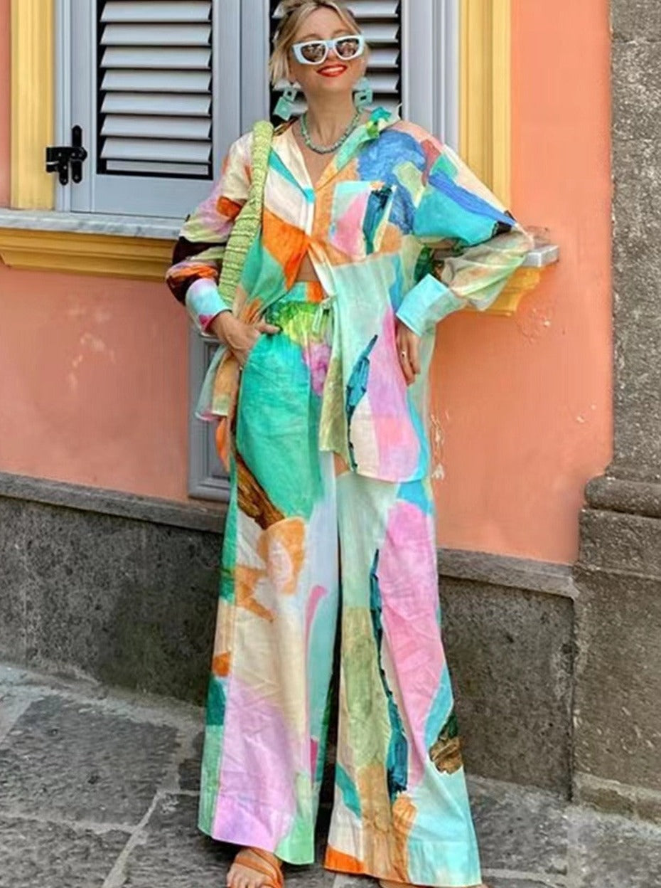 Frau in farbenfrohem, abstraktem Zweiteiler vor pastellfarbener Wand, modisch, Sommeroutfit, Streetstyle, trendige Damenmode, auffällige Muster.