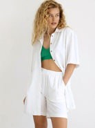 Frau in weißem Hemd und Shorts, grünes Top, lockiges Haar. Sommermode, lässiger Look, stilvolle Damenbekleidung, trendige Outfits.