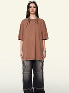 Braunes Oversize-T-Shirt, kombiniert mit weiten, dunklen Jeans und Ketten-Accessoires. Trendige Streetwear für Damen, lässiger Look.