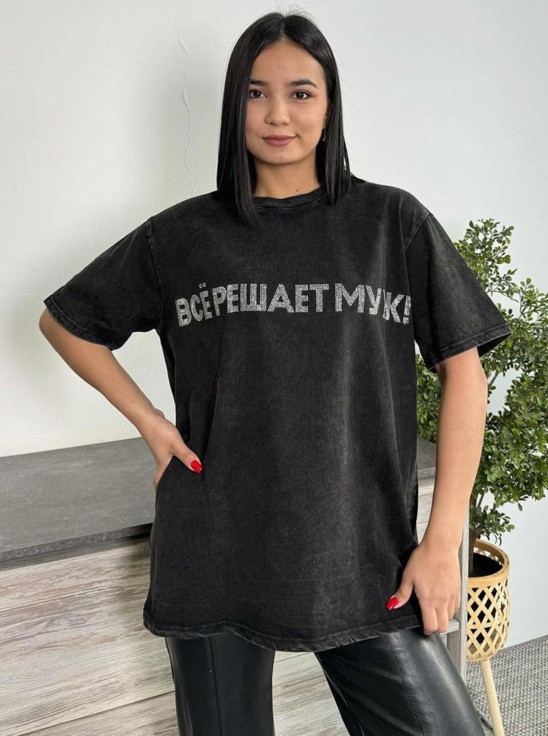 Frau trägt schwarzes Oversize-T-Shirt mit russischem Schriftzug, kombiniert mit Lederhose. Modetrend, Streetwear, lässiger Stil, Damenmode.