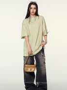 Frau in übergroßem, grünem T-Shirt und zerrissenen Jeans, hält eine braune Handtasche. Modetrend, Streetwear, lässiger Stil, Damenmode.